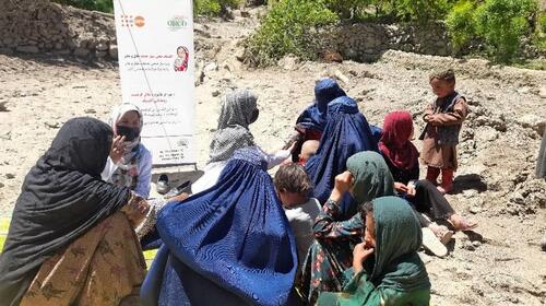 Un groupe de femmes et d’enfants discutent à l’extérieur, assis sur un terrain rocheux